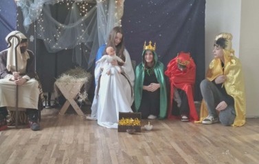 Uczniowie podczas przedsatwienia jasełek: W stajence przy żłobie siedzą w przebraniach J&oacute;zef i Maryja trzymająca na kolanach Jezusa. Obok po prawej stronie trzech kr&oacute;li klęczy z darami w dłoniach.