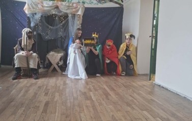 Uczniowie podczas przedsatwienia jasełek: W przebraniach siedzą w stajence Maryja z J&oacute;zefem, między kt&oacute;rymi stoi żłobek z dzieciątkiem. Po prawej stronie w przebraniach trzech kr&oacute;li przyklęka i trzyma dary.