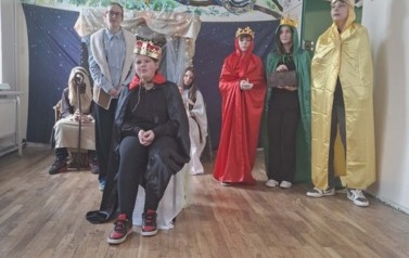 Uczniowie podczas przedsatwienia jasełek: W przebraniach siedzą w stajence Maryja z J&oacute;zefem, między kt&oacute;rymi stoi żłobek z dzieciątkiem. Po prawejj stoi w przebraniach trzech kr&oacute;li trzymający dary. Na środku siedzi Herod na krześle.