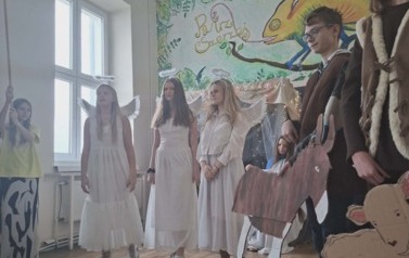 Uczniowie podczas przedsatwienia jasełek: W przebraniach Maryja z lewej strony, stoi w przebraniach trzy anioły, z prawej dwaj pasterze trzymają tekturowe owieczkę i osiołka