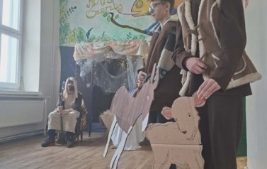 Uczniowie podczas przedsatwienia jasełek: W przebraniach w stajence siedzi J&oacute;zef, z prawej dwaj pasterze z makietami owcy i osiołka 