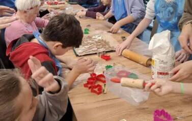 Grupa dzieci i senior&oacute;w siedząca przy stole podczas spotkania świątecznego, wykonują dekoracje świąteczne