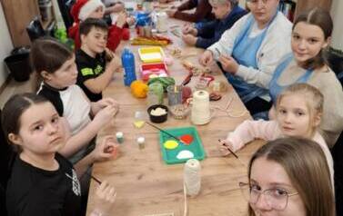 Grupa dzieci i senior&oacute;w siedząca przy stole podczas spotkania świątecznego wykonują dekoracje świąteczne