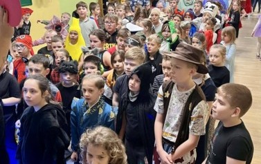 Duża grupa dzieci i nauczyciele w przebraniach za r&oacute;żne postacie podczas balu karnawałowego i wsp&oacute;lnej zabawy w sali gimnastycznej