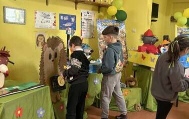 Grupa uczni&oacute;w na szkolnym korytarzu oglądajaca prace konursowe przygotowane na paradę jeża