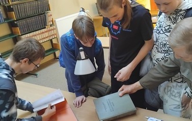 Grupa uczni&oacute;w w bibliotece Instytutu Fizyki Uniwersytetu Ł&oacute;dzkiego ogląda pozycje książkowe