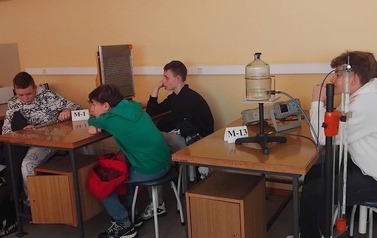 Uczniowie siedzą przy wyposażonych w pomoce dydaktyczne stolikach w sali Instytutu Fizyki Uniwersytetu Ł&oacute;dzkiego