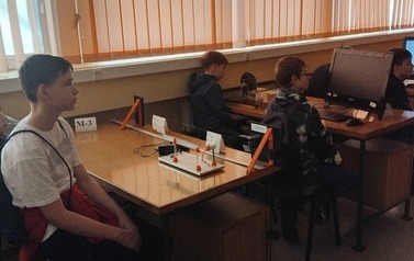 Uczniowie siedzą przy wyposażonych w pomoce dydaktyczne stolikach w sali Instytutu Fizyki Uniwersytetu Ł&oacute;dzkiego
