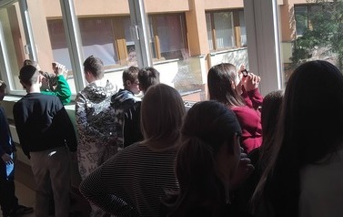 Uczniowie stoją w oknach na korytarzu Instytutu Fizyki Uniwersytetu Ł&oacute;dzkiego i oglądają przez specjalne okulary słońce