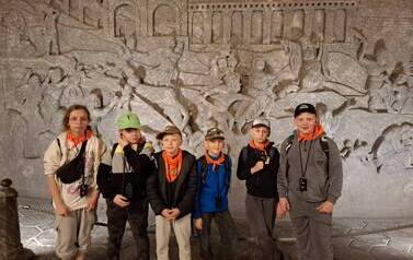 Grupa uczni&oacute;w pozuje do zdjęcia na tle ściany z płaskorzeźbami w soli w koalni w Wieliczce