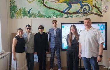 Troje uczni&oacute;w wraz z dwoma opiekunami stoi na tle ektranu monitora z wyświetlonym tytułem prezentowanego projektu. Obok monitora duża makieta ze środkami uzależniającymi i ich opisem.