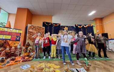 Grupa dzieci podczas przedstawienia "Gdzie jest jest jeż?" na tle dekoracji z kolorowych jesiennych liści, dyni i owoc&oacute;w jesieni
