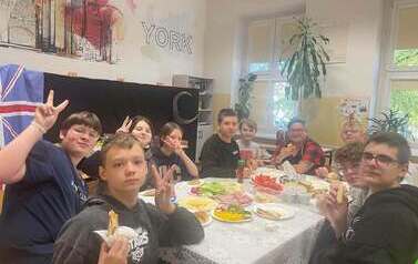Grupa uczni&oacute;w w sali lekcyjnej, siedzi wok&oacute;ł nakrytego stołu podczas zdrowego śniadania