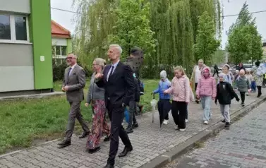 Duża grupa dzieci idąca chodnikiem przed szkołą podczas parady. Na czele grupy idą Prezydent Miasta, naczelnik oświaty i dyrektor szkoły.