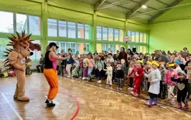 Duża grupa dzieci i opiekun&oacute;w tańczy w sali gimnastycznę podczas zakończenia imprezy Parada jeża ze Zgierza. Na śrdoku stoi nauczycielka w pomarańczowych spodniach, czarnej bluzce i czarnej czapeczce prowadzi taniec zumbę, zachęca dzieci do zabawy. Obok s