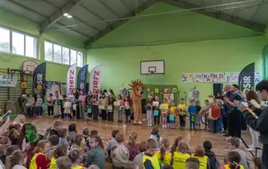 Duża grupa dzieci na sali gimnastycznej oklskuje nagrodzoną grupę dzieci stojącą na środku. 