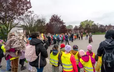 Grupa dzieci stojąca na Placu 100 Straconych, ustawiona w literę u. Dzieci w kolorowych strojach, trzymają jeże kukiełki plakaty z jeżem. W środku dyrektor szkoły przemawia do dzieci.