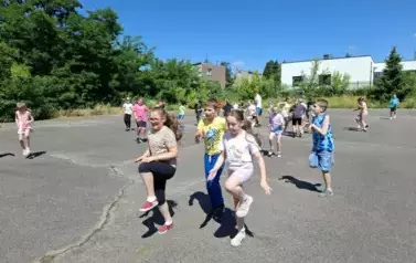 Grupa uczni&oacute;w na boisku szkolnym wykonująca pokazywane przez opiekuna ćwiczenia