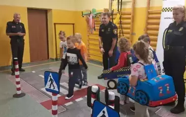 Grupa uczni&oacute;w pokonuje tor ruchu drogowego. Pan i pani w mundurach Straży Miejskiej nadzorują prawidłowe wykonanie zadań.