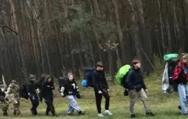 Grupa młodych ludzi wędrujaca lasem po Puszczy Kampinowskiej na polanę z cmentrzem w Palmirach
