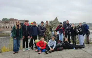 Grupa uczni&oacute;w pozuje do zdjęcia na tle rzeki Narwi i widocznych w tle ruin budynku