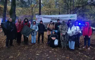 Grupa uczni&oacute;w stojąca w lesie na tle baneru z napisem: "Centralny Zlot Młodzieży Palmiry".