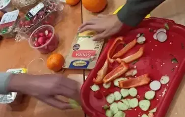 Uczniowie w sali lekcyjnej siedzą przy stolikach, na kt&oacute;rych rozłożono r&oacute;żne produkty (owoce, warzywa, soki, serki, pieczywo chrupkie, inne) do przygotowania zdrowego śniadania