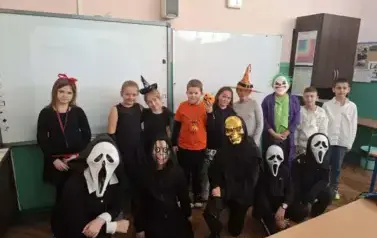 Grupa uczni&oacute;w w sali lekcyjnej w przebraniach halloweenowych pozuje do zdjęcia.