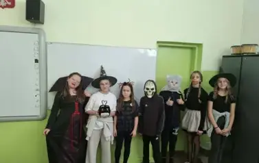 Grupa uczni&oacute;w w sali lekcyjnej w przebraniach halloweenowych pozuje do zdjęcia.