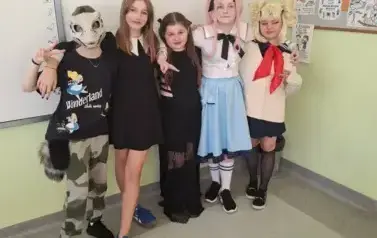 Grupa uczni&oacute;w w sali lekcyjnej w przebraniach halloweenowych pozuje do zdjęcia.