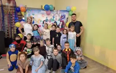 Duża grupa dzieci w przebraniach za postacie z bajek, pozuje do zdjęcia na tle dekoracji: duża tablica z posyaciami z bajek.