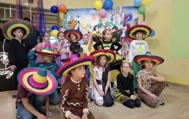 Duża grupa dzieci w przebraniach za postacie z bajek, pozuje do zdjęcia na tle dekoracji: duża tablica z posyaciami z bajek.