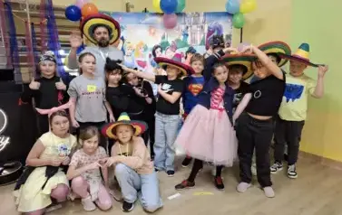 Duża grupa dzieci w przebraniach za postacie z bajek, pozuje do zdjęcia na tle dekoracji: duża tablica z posyaciami z bajek.