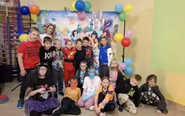 Duża grupa dzieci w przebraniach za postacie z bajek, pozuje do zdjęcia na tle dekoracji: duża tablica z posyaciami z bajek.