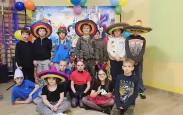 Duża grupa dzieci w przebraniach za postacie z bajek, pozuje do zdjęcia na tle dekoracji: duża tablica z posyaciami z bajek.