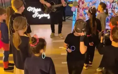 Duża grupa dzieci w przebraniach za postacie z bajek tańczy w sali gimnastycznej.