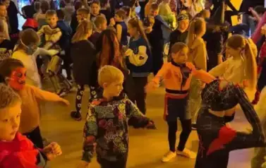 Duża grupa dzieci w przebraniach za postacie z bajek tańczy w sali gimnastycznej.