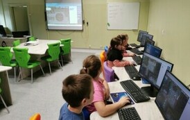 Uczniowie siędzący przy stolikach przed laptopami