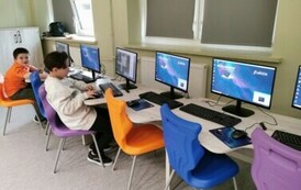 Uczniowie siędzący przy stolikach przed laptopami