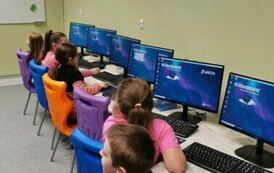 Uczniowie siędzący przy stolikach przed laptopami