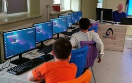 Uczniowie siędzący przy stolikach przed laptopami