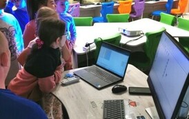 Uczniowie siędzący przy stolikach przed laptopami