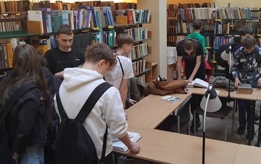 Grupa uczni&oacute;w w bibliotece Instytutu Fizyki Uniwersytetu Ł&oacute;dzkiego ogląda pokazywane przez prowadzącego pozycje książkowe
