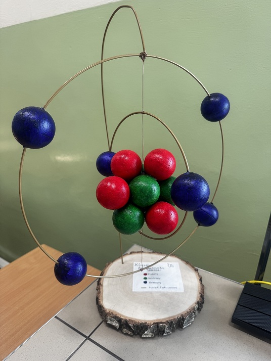 Model atomu z&nbsp;kolorowych kulek na&nbsp;stojaku na&nbsp;drewnianej podstawce