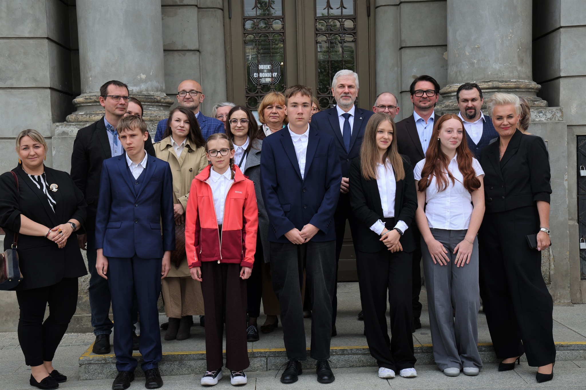 Grupa uczni&oacute;w i&nbsp;opiekun&oacute;w pozuje do zdjęcia przed Archiwum Państwowym w&nbsp;Łodzi, w&nbsp;towrzystwie kuratora oświaty, dyrektora archiwum i&nbsp;os&oacute;b towarzyszących, po rozdaniu nagr&oacute;d w&nbsp;konkursie