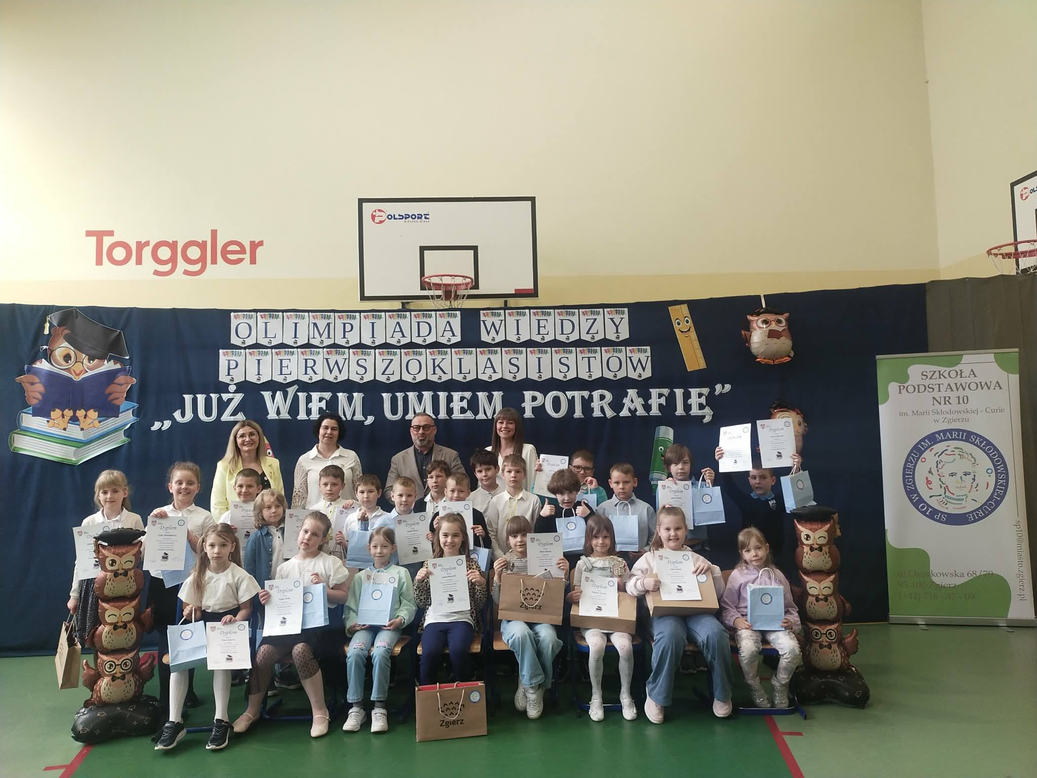 Duża grupa dzieci pozuje do zdjęcia z&nbsp;dyrektorem szkoły i&nbsp;prezydentem miasta na&nbsp;tle dużego napisu informującego o&nbsp;tytule konkursu