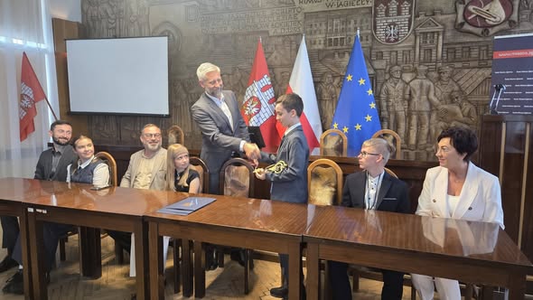 Prezydent miasta z&nbsp;grupą dzieci w&nbsp;sali obrad UMZ Zgierza, ściska dłoń uczniowi - skarbnikowi