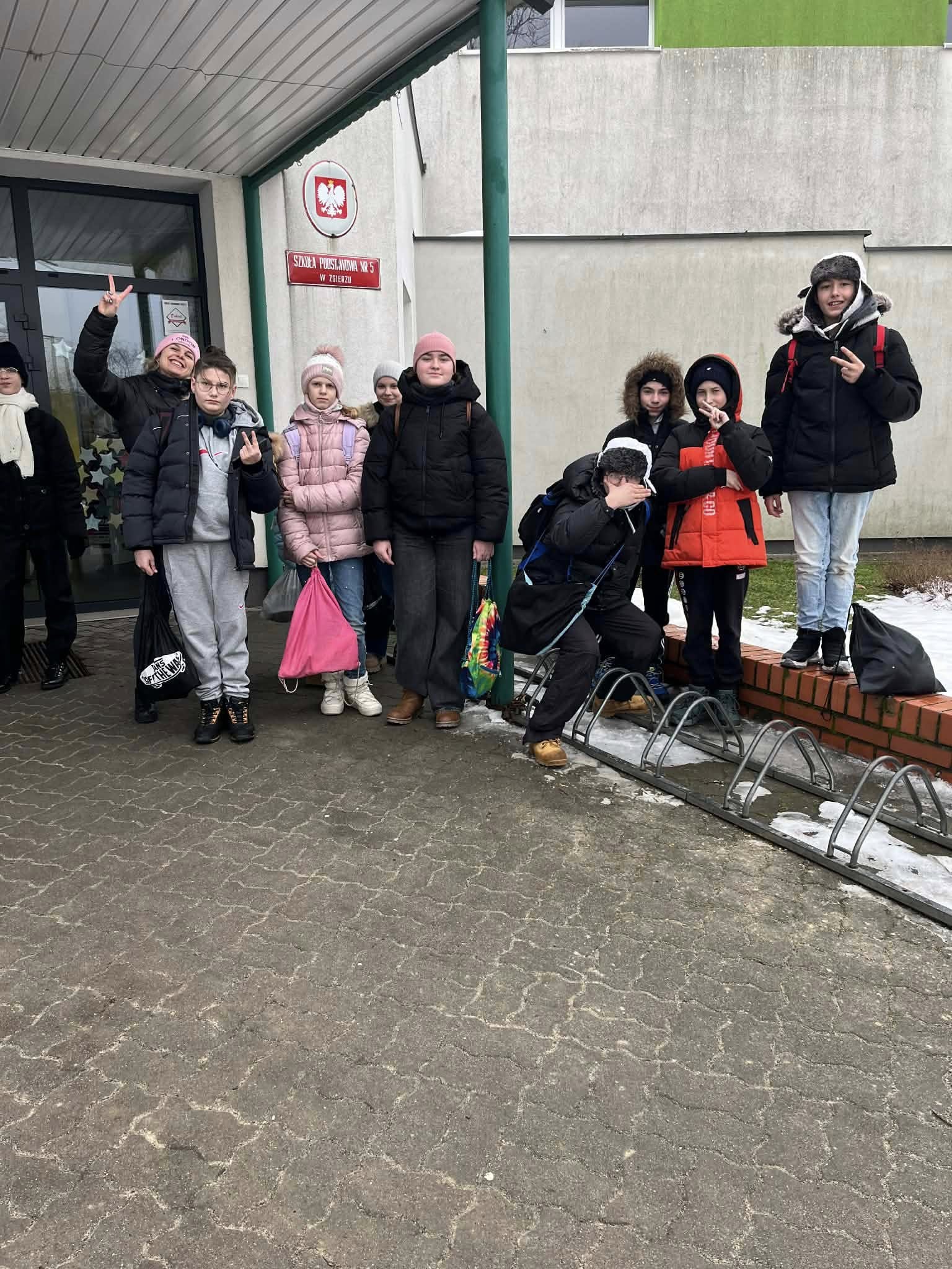 Grupa uczni&oacute;w pozuje do zdjęcia przed budynkiem szkoły w&nbsp;czasie rajdu WOŚP