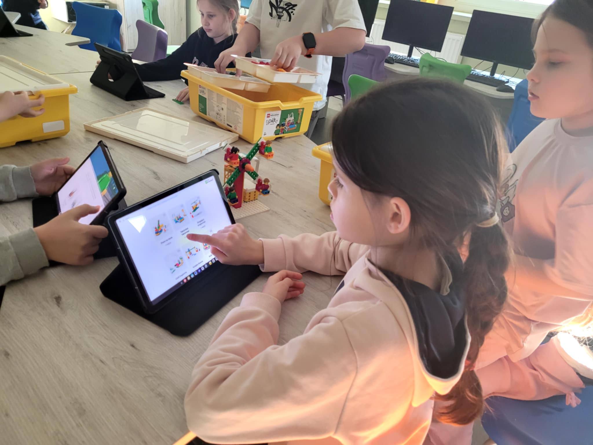Dziewczynka siedzi przy stole z&nbsp;uruchomionym tabletem i&nbsp;klockami Lego