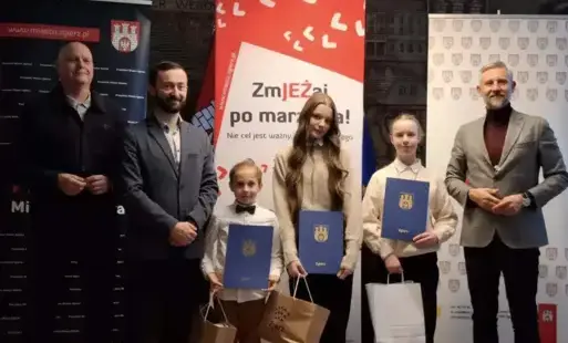 Trzech uczniów po odebraniu nagród za osiągnięcia sportowe, pozuje do zdjęcia  w sali urzędu miasta na tle banerów reklamujących impreze. Po lewej stronie stoi dwóch przedstawicieli UM a po prawej Prezydent miasta. 